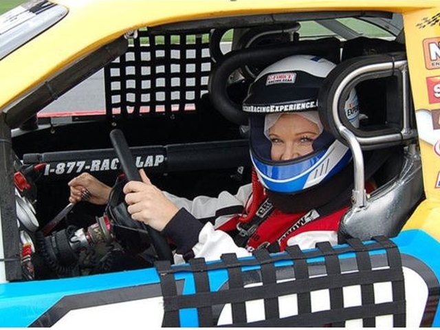 A driver in a helmet behind the wheel of a stock car