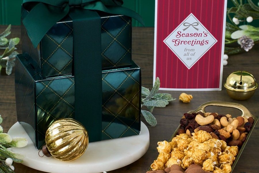 Stacked holiday gift boxes beside nuts, caramel corn and chocolates